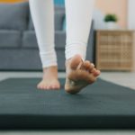 Low shot slow motion of a woman rolling out yoga mat then working out in plank position
